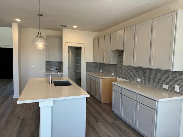 kitchen featuring sink, gray cabinets, dark wood-type flooring, a kitchen island with sink, and decorative light fixtures