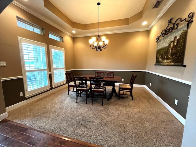 dining space featuring dark colored carpet, a raised ceiling, ornamental molding, and a chandelier