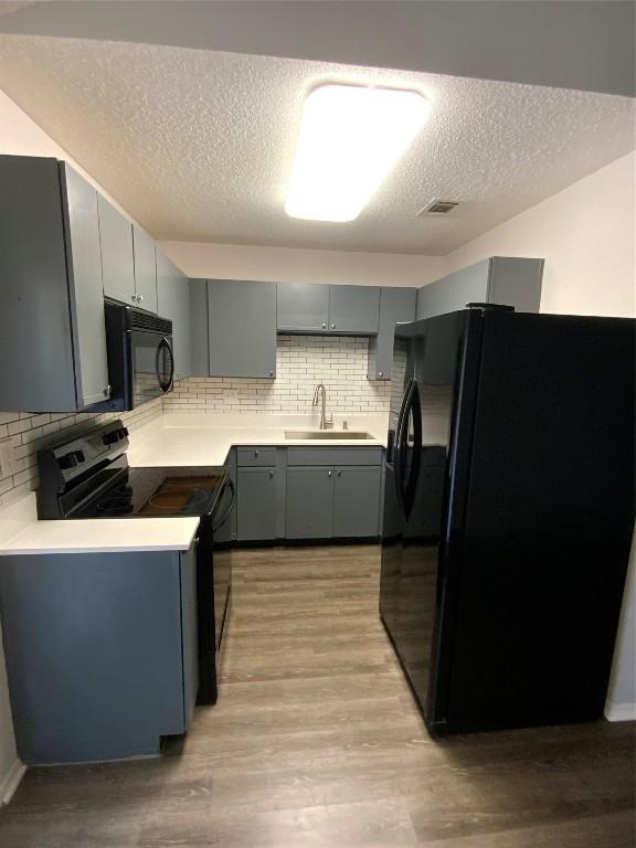 kitchen with tasteful backsplash, sink, black appliances, and light hardwood / wood-style floors