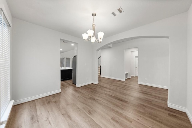 unfurnished dining area with a notable chandelier, wood-type flooring, and vaulted ceiling