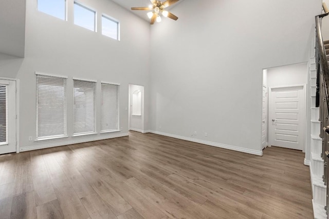 unfurnished living room with ceiling fan, a high ceiling, and light hardwood / wood-style flooring