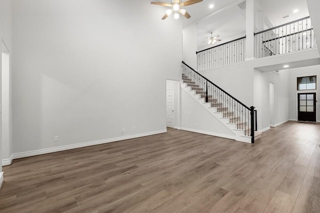 unfurnished living room featuring ceiling fan, hardwood / wood-style floors, and a towering ceiling