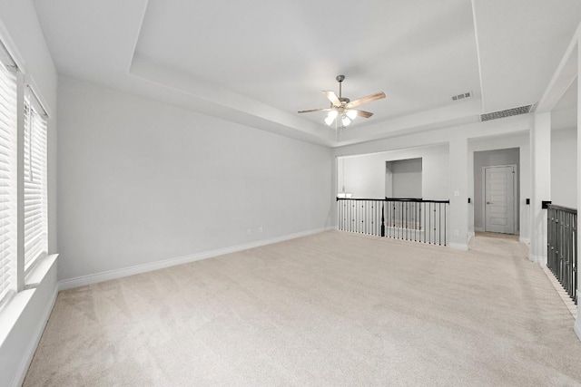 empty room with light colored carpet, a raised ceiling, and ceiling fan