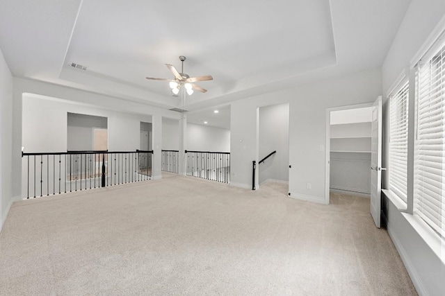 carpeted empty room with a raised ceiling and ceiling fan