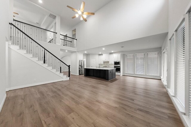 unfurnished living room with high vaulted ceiling, wood-type flooring, and ceiling fan