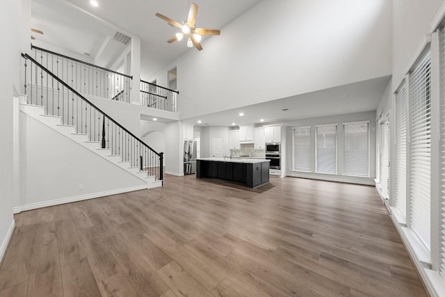 unfurnished living room with hardwood / wood-style flooring, ceiling fan, and a towering ceiling