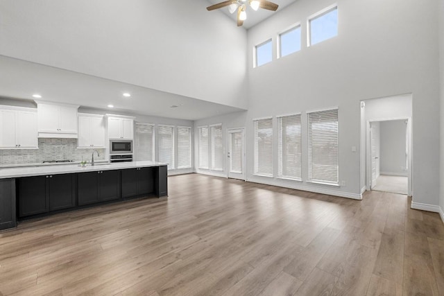 unfurnished living room with a high ceiling, light hardwood / wood-style floors, ceiling fan, and sink