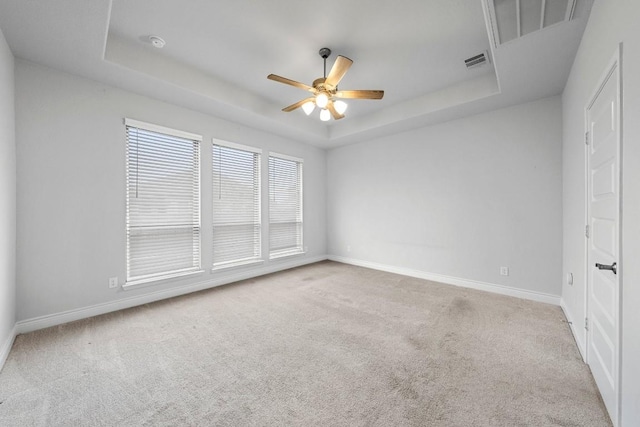 empty room with light carpet, a raised ceiling, and ceiling fan