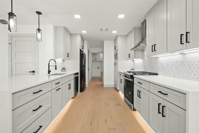 kitchen featuring wall chimney exhaust hood, decorative light fixtures, stainless steel gas stove, sink, and light wood-type flooring