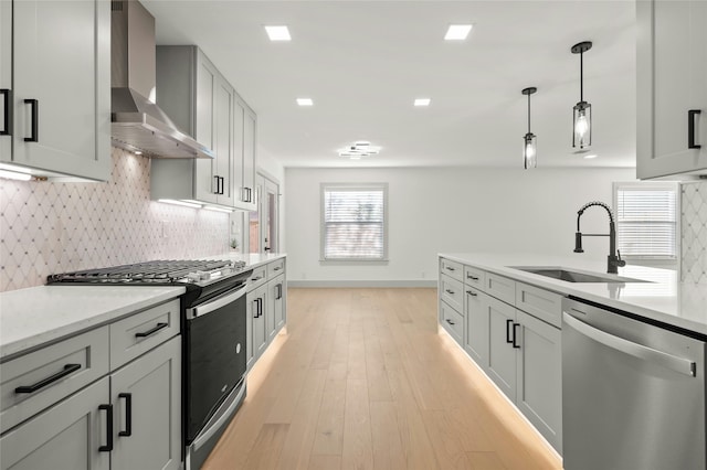 kitchen featuring wall chimney exhaust hood, stainless steel appliances, decorative backsplash, sink, and gray cabinetry