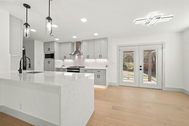 kitchen featuring wall chimney range hood, french doors, sink, backsplash, and stainless steel stove