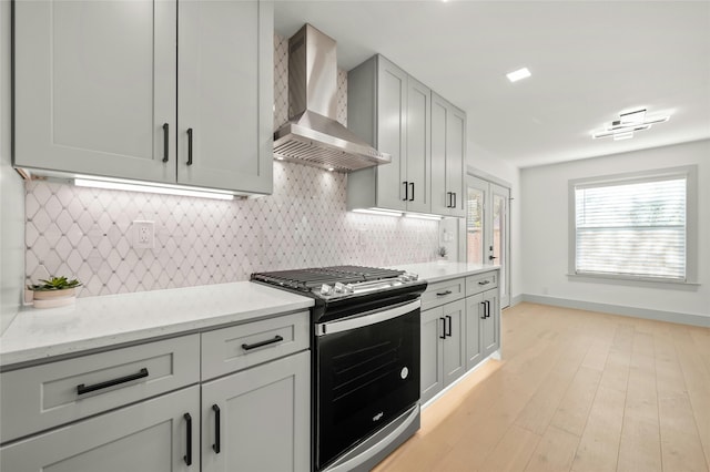 kitchen featuring light stone countertops, wall chimney range hood, gas stove, and tasteful backsplash