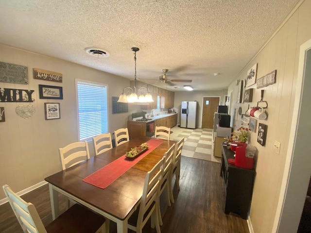 dining area with a textured ceiling, ceiling fan with notable chandelier, and dark hardwood / wood-style floors