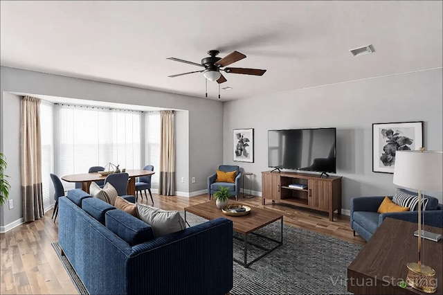 living room featuring baseboards, a ceiling fan, visible vents, and light wood-style flooring