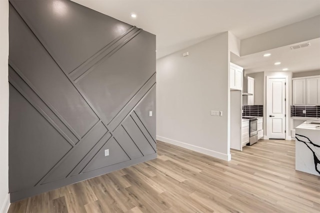 interior space featuring backsplash, light hardwood / wood-style floors, white cabinetry, and stainless steel electric stove