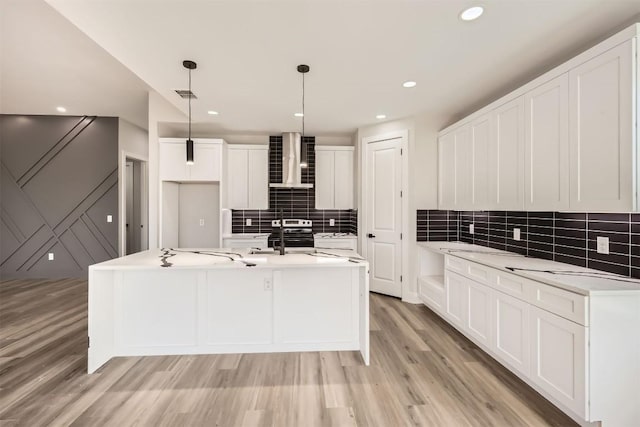 kitchen featuring pendant lighting, a center island with sink, wall chimney range hood, and light hardwood / wood-style flooring