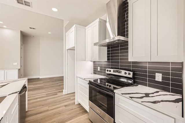 kitchen with wall chimney exhaust hood, appliances with stainless steel finishes, decorative backsplash, white cabinets, and light wood-type flooring