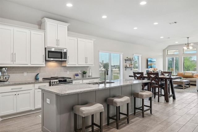 kitchen with backsplash, a center island with sink, white cabinetry, a breakfast bar area, and stainless steel appliances