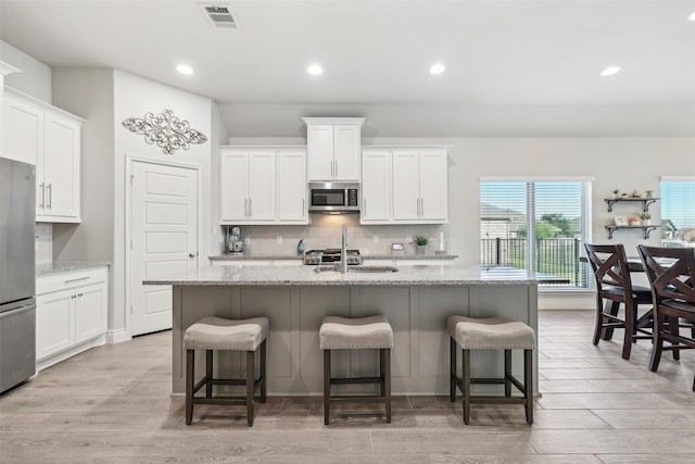 kitchen featuring a kitchen island with sink, light stone countertops, appliances with stainless steel finishes, a kitchen breakfast bar, and white cabinets