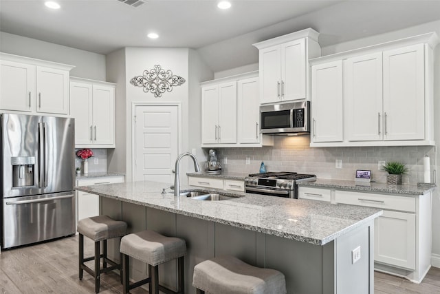 kitchen with an island with sink, sink, stainless steel appliances, and white cabinetry