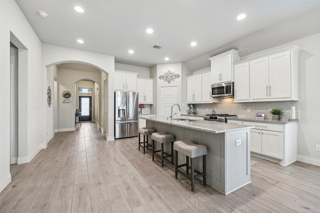 kitchen featuring light stone countertops, white cabinets, stainless steel appliances, and a kitchen island with sink