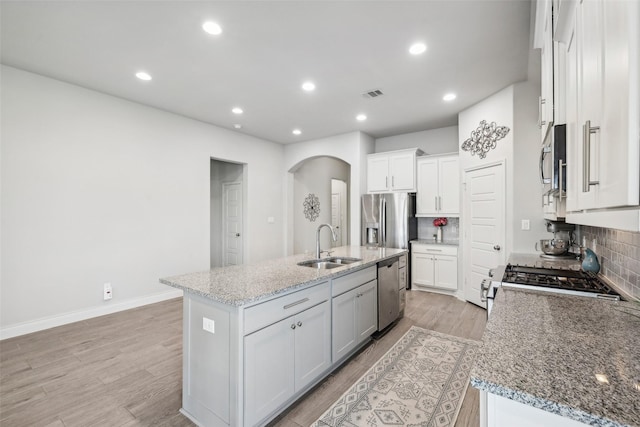 kitchen featuring light stone countertops, white cabinetry, decorative backsplash, sink, and a center island with sink