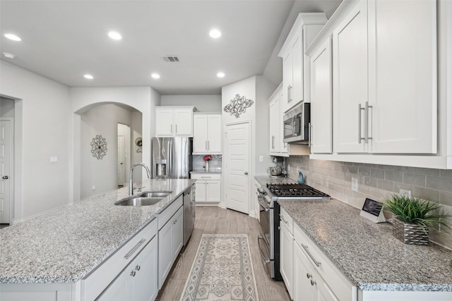 kitchen with appliances with stainless steel finishes, white cabinetry, an island with sink, sink, and light stone counters