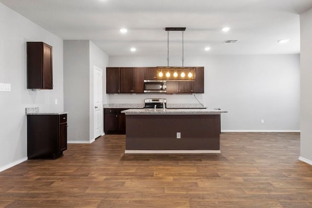 kitchen featuring light stone countertops, stainless steel appliances, dark wood-type flooring, decorative light fixtures, and a center island with sink