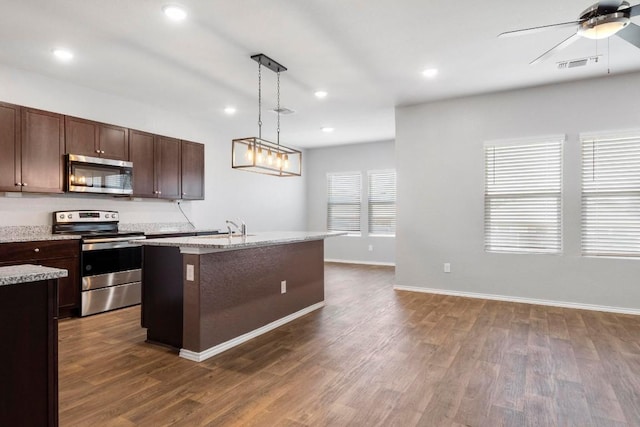 kitchen with appliances with stainless steel finishes, a kitchen island with sink, dark wood-type flooring, ceiling fan, and hanging light fixtures