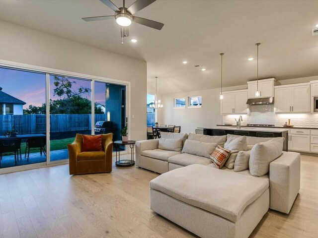 living room featuring light hardwood / wood-style flooring, ceiling fan with notable chandelier, and sink