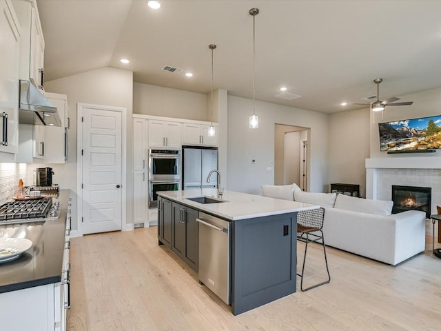 kitchen featuring appliances with stainless steel finishes, a kitchen island with sink, sink, white cabinetry, and hanging light fixtures