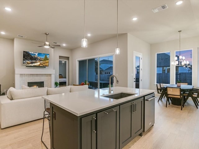 kitchen with light wood-type flooring, a center island with sink, hanging light fixtures, and sink