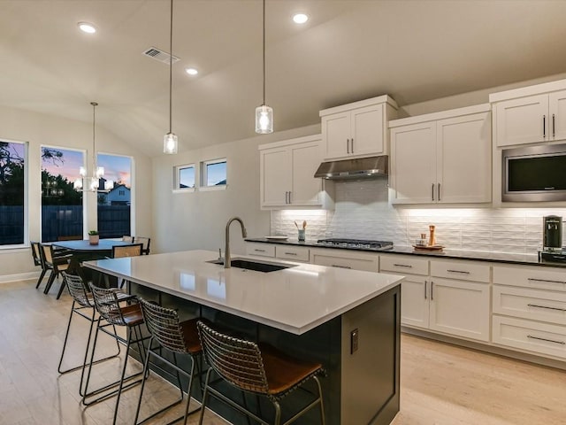 kitchen with pendant lighting, vaulted ceiling, stainless steel appliances, and an island with sink