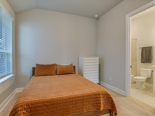 bedroom featuring light hardwood / wood-style flooring, ensuite bath, and lofted ceiling