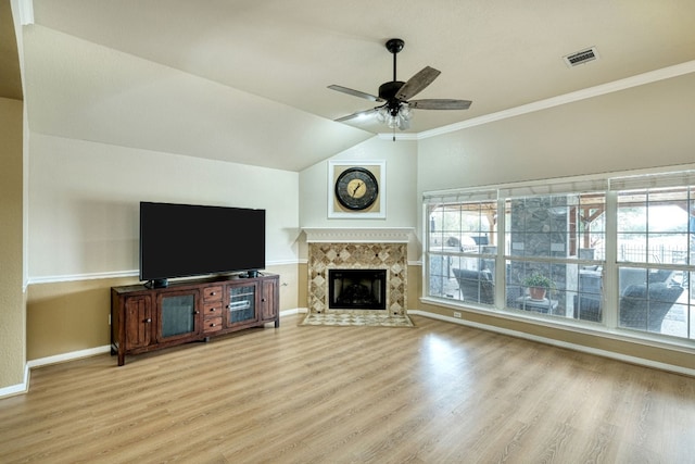 unfurnished living room featuring crown molding, vaulted ceiling, ceiling fan, light wood-type flooring, and a tiled fireplace