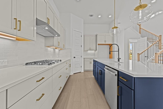 5900 Comanche Moon Trl, Austin, TX 78747 - kitchen with blue cabinetry, under cabinet range hood, appliances with stainless steel finishes, light countertops, and white cabinetry