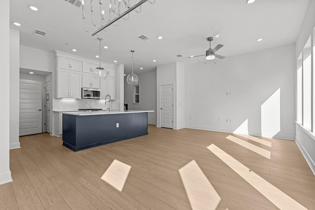 kitchen featuring a kitchen island with sink, visible vents, light countertops, light wood finished floors, and stainless steel microwave