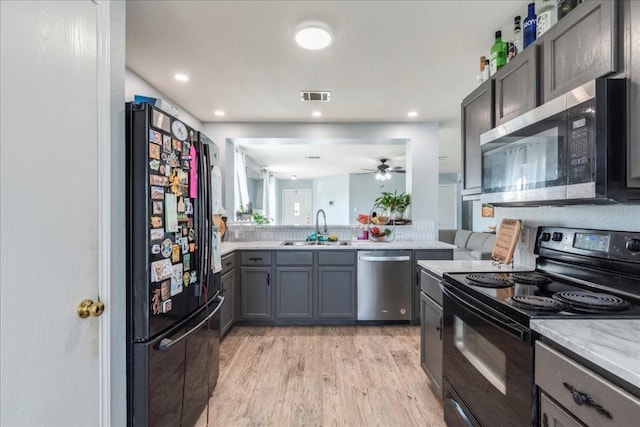 kitchen with black appliances, sink, light hardwood / wood-style flooring, ceiling fan, and light stone counters