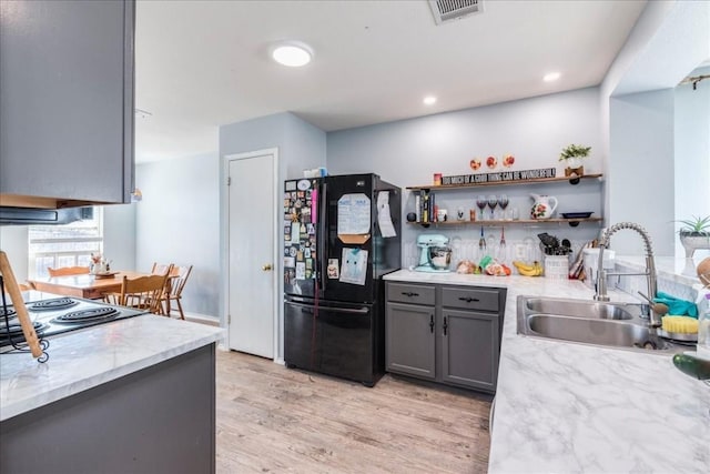 kitchen with gray cabinetry, black refrigerator, light hardwood / wood-style floors, and sink