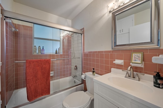 full bathroom with combined bath / shower with glass door, vanity, toilet, and tile walls