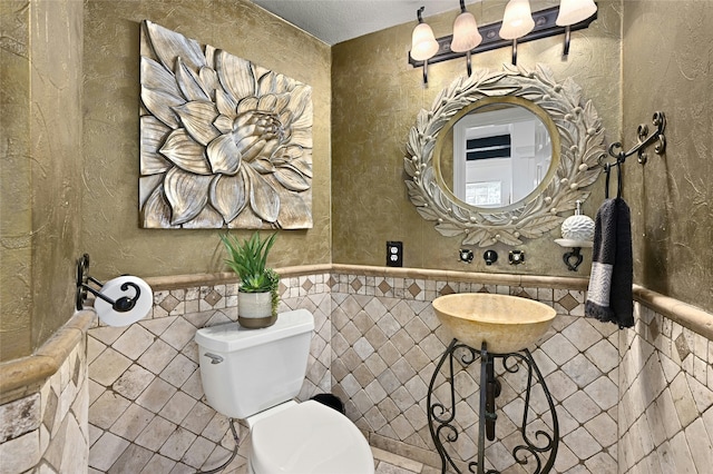 bathroom with a textured ceiling, toilet, and tile walls