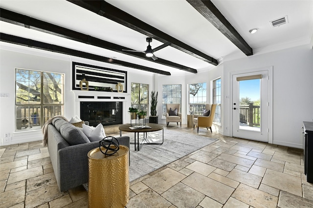 living room featuring stone tile flooring, a glass covered fireplace, plenty of natural light, and baseboards