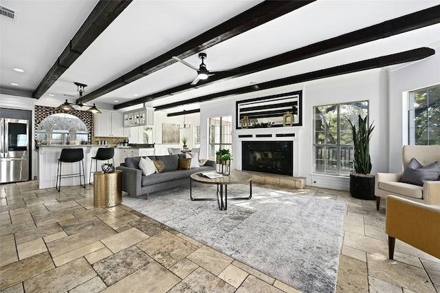 living room with beam ceiling, a tile fireplace, and ceiling fan