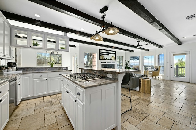 kitchen featuring a breakfast bar, ceiling fan, beam ceiling, a center island, and white cabinetry