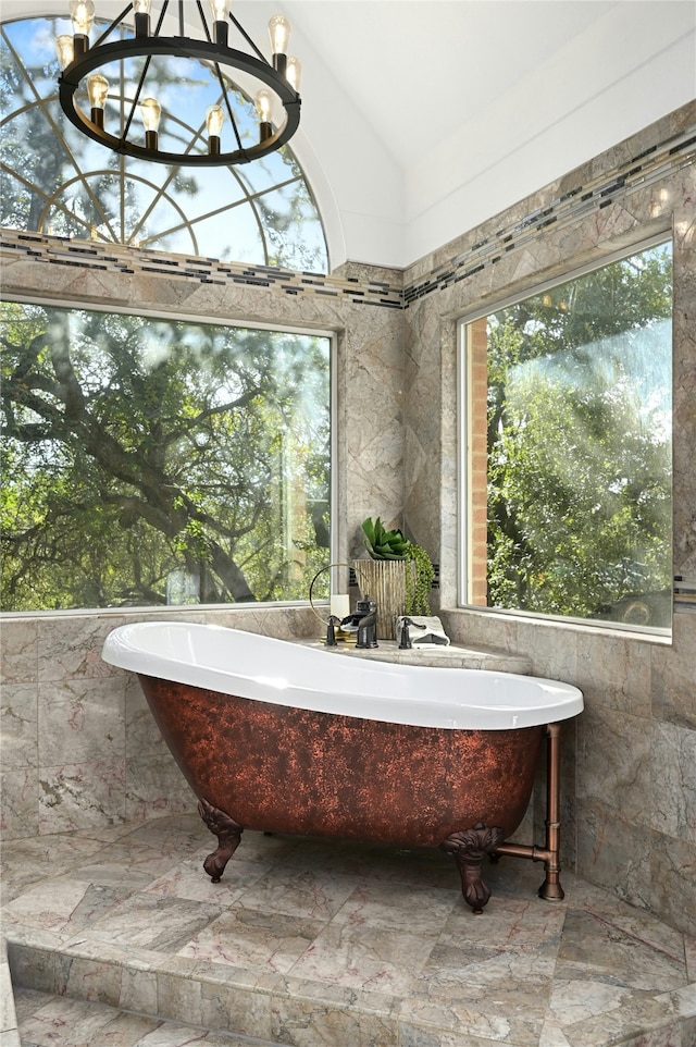 bathroom featuring a notable chandelier, a bathtub, lofted ceiling, and tile walls