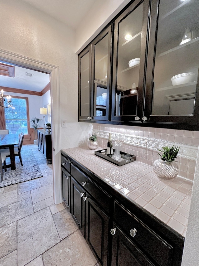 interior space with stone tile floors, visible vents, an inviting chandelier, ornamental molding, and backsplash