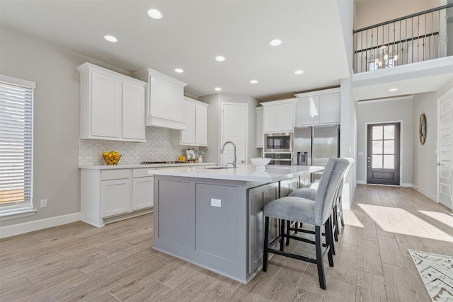 kitchen with a breakfast bar, stainless steel appliances, light hardwood / wood-style flooring, white cabinets, and an island with sink