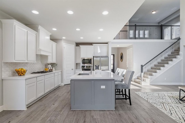 kitchen with sink, light hardwood / wood-style floors, a center island with sink, white cabinets, and appliances with stainless steel finishes