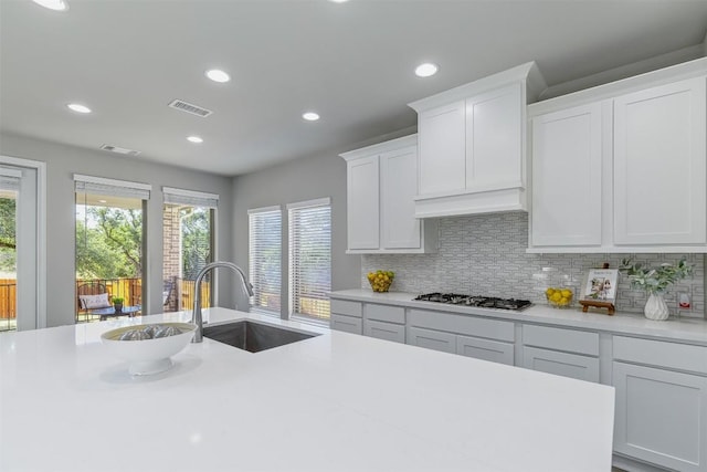 kitchen with tasteful backsplash, custom exhaust hood, stainless steel gas cooktop, sink, and white cabinets