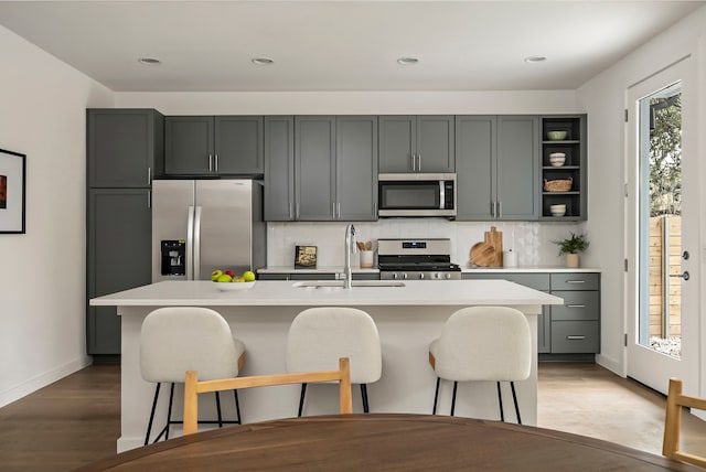 kitchen with stainless steel appliances, an island with sink, decorative backsplash, sink, and gray cabinets